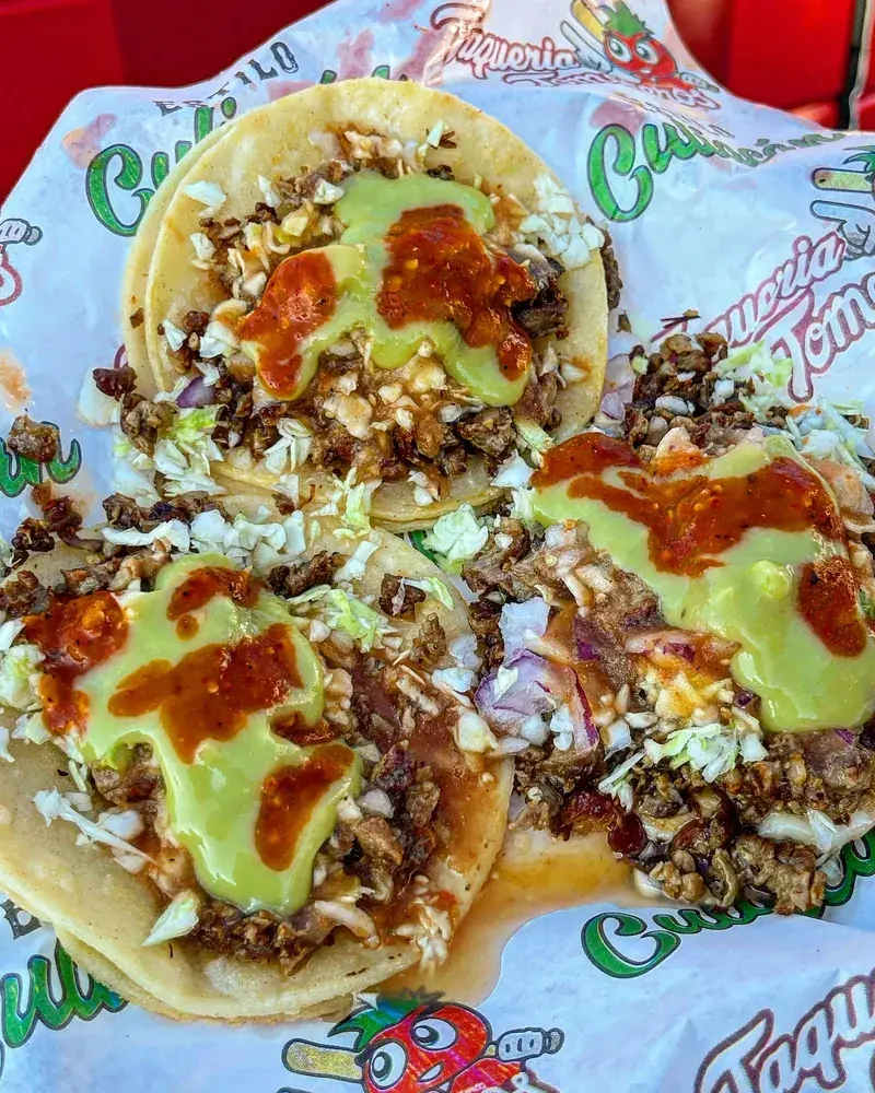 Three street tacos with chopped meat, cabbage, onion and salsa