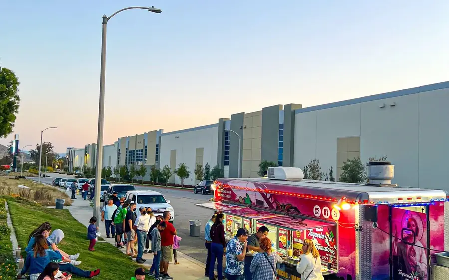 The Taqueria Tomateros trailer lit up at dusk with customers waiting